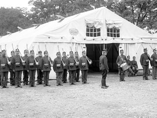 Schwarzweiss-Foto: Soldaten stehen vor einem grossen, weissen Zelt in Formation.