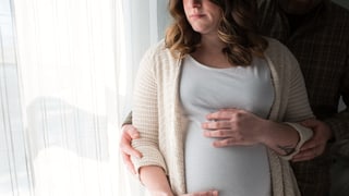 Eine schwangere Frau hält ihren Bauch. Ihr Partner hält ihren Arm. Eine schwangere Frau hält ihren Bauch. Ihr Partner hält ihren Arm.