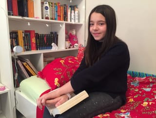 Ein Mädchen sitzt auf dem Bett und hält ein Buch und lacht