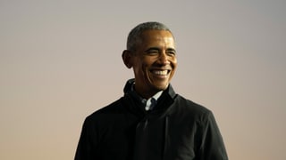 Präsident Obama trägt einen schwarzen Mantel und grinst nach rechts.