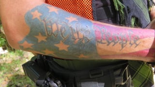 Eine Tätowierung auf dem Arm eines Milizionärs. Sie zeigt die US-Flagge mit der Aufschrift «We the People»