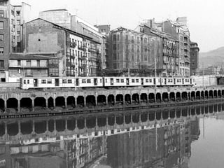 Zug steht am Ufer des Flusses, dahinter vierstöckige Wohnhäuser
