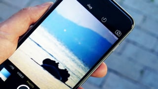 Eine Hand hält ein Smartphone. Darauf ist die Kamera-App zu sehen, das Bild zeigt ein Schlauchboot auf einem Meer.