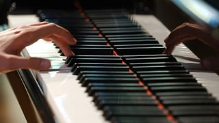 Blick auf die Tasten eines Klaviers, die gespielt werden, allerdings nur von einer linken Hand.