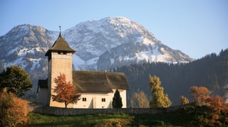 Die Kirche Temple de Château-d'Oex auf einer grünen Anhöhe vor verschneiten Bergen.