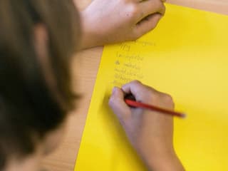 Ein Mädchen schreibt auf ein gelbes Blatt Schulaufgaben.