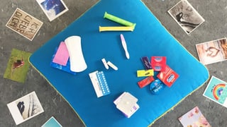 Auf einem kissen liegen Kondome, ein Schwangerschaftstest, Binden, Tampons und Pillen. Auf einem kissen liegen Kondome, ein Schwangerschaftstest, Binden, Tampons und Pillen.