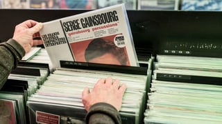 Eine Kiste mit Schallplatten in einem Laden. Jemand zieht ein Album von Serge Gauinsbourg heraus.