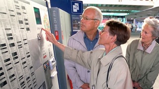 Drei ältere Personen bedienen zusammen einen Billett-Automat.
