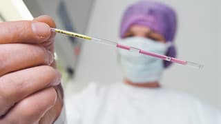 Eine Klinikangestellte hält ein Röhrchen mit befruchteten Eizellen in der Hand.