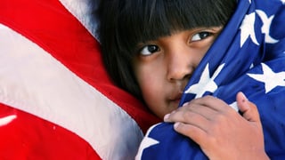 Ein Kind mit hispano-amerikanischem Aussehen schmiegt sich an eine US-Flagge. 