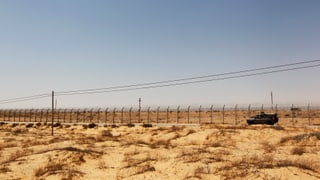Ein Fahrzeug fährt einen Grenzzaun entlang, dahinter die Wüste Sinai.