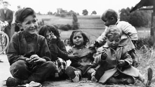 Kinder, die am Boden sitzen, auf einer historischen Aufnahme.