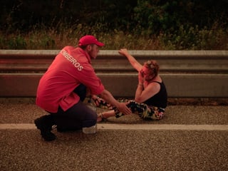 Ein Feuerwehrmann hilft einer Frau, die auf der Strasse sitzt.