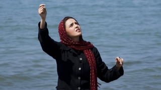 Ein Mädchen mit rotem Kopftuch spannt eine Anglerschnur, im Hintergrund das Meer.