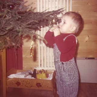 Ein kleiner Bub mit rotem Pullover und karierter Hose nascht Schokolade von einem Weihnachtsbaum.