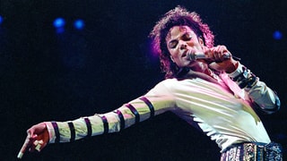 Michael Jackson während eines Konzerts: den Oberkörper zurückgelehnt, den rechten Arm ausgestreckt, links hält er das Mikrofon. 