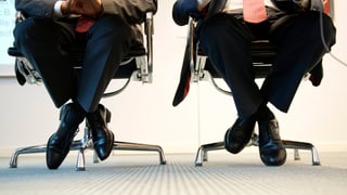 Zwei Männer in Anzügen sitzen auf Bürostühlen. Zwei Männer in Anzügen sitzen auf Bürostühlen.