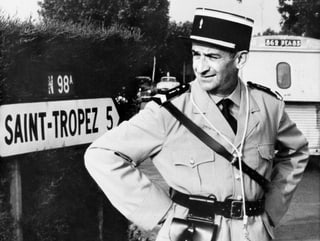 De Funès steht als Polizist vor einem Ortsschild von Saint Tropez.