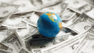 Eine kleine Weltkugel liegt auf Dollar-Noten