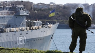 Ein Soldat steht beim Hafen mit Blick auf ein Kriegsschiff.