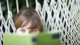 Eine Frau liest ein Buch in einer Hängematte.