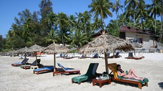 Eine Touristin liegt an einem von Palmen gesäumten Strand in Burma.