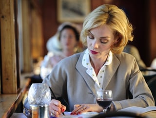 Filmszene aus «Verliebte Feinde». Mona Petri sitzt als Juristin Iris von Roten im Restaurant bei einem Glas Wein und macht sich Notizen.