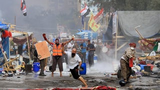 Menschen schleudern Gegenstände, im Hintergrund zerfallene Protestcamps.
