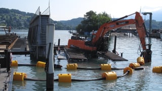 Ein Bagger, der auf einem Ponton im See steht, baggert Schlacke vom Seegrund. Ein Bagger, der auf einem Ponton im See steht, baggert Schlacke vom Seegrund.