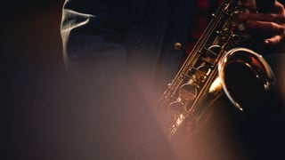 Jemand spielt Saxophon im Halbdunkeln der Bühne