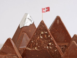 Ein aus Toblerone-Stücken geformtes Gebirge mit Schweizer Flagge auf dem Schokolade-Gipfel.