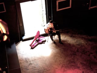 In einem grossen Raum sitzt Philipp Fankhauser mit seiner Gitarre auf einem einfach Stuhl. Daneben liegt der geöffnete Gitarrenkoffer.
