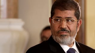 Mohammed Mursi, wie er zur Seite blickt. Er trägt Anzug und Brille. 