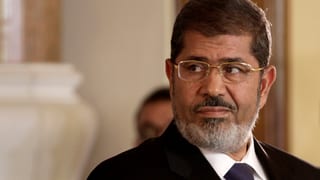 Mohammed Mursi, wie er zur Seite blickt. Er trägt Anzug und Brille. Mohammed Mursi, wie er zur Seite blickt. Er trägt Anzug und Brille.