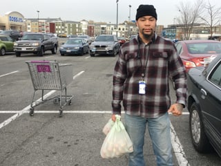Mann mit Lebensmitteln in der Hand auf einem Parkplatz