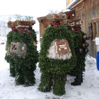 Mehrere mit Tannenzweigen und Hauben geschmückte Personen stehen im Schnee im Kreis. Mehrere mit Tannenzweigen und Hauben geschmückte Personen stehen im Schnee im Kreis.