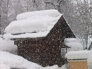 Auf einer Hütte am Hang liegt ein Meter Schnee, es schneit stark.