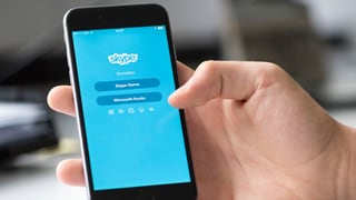Eine Hand hält ein Handy, auf dem die Icons der WhatsApp und der Skype-App zu sehen sind.