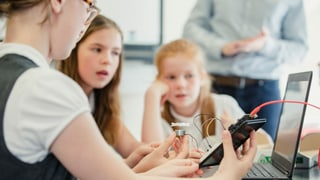 Mädchen an einem Tisch mit einem Handy und Kabeln in der Hand. Mädchen an einem Tisch mit einem Handy und Kabeln in der Hand.