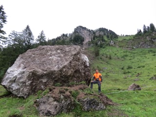 Ein Mann mit orangem Oberteil steht neben einem fast haushohen Felsblock.