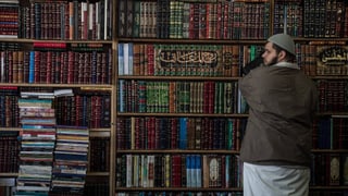 Ein Moslem steht vor einem Gestell voller islamischer Bücher.