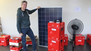 Mann hält Solarpanel, rote Kisten daneben. Mann hält Solarpanel, rote Kisten daneben.