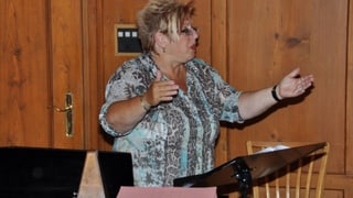 Die blondhaarige Frau mit Brille zeigt mit hochgehaltenen Armen eine typische Dirigenten-Pose.
