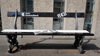 Eine schwarze Sitzbank mit weisser Aufschrift der BKB vor dem Bankgebäude in Riehen.