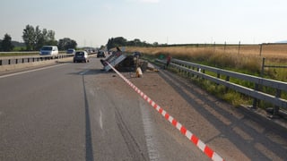 Der Anhänger liegt umgekippt halb auf der Rechten Spur, halb auf dem Pannenstreifen. Im Vordergrund liegt Kies auf der Strasse. Die Situation ist mit einem Absperrband vom restlichen Verkehr getrennt. 