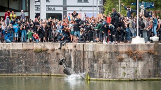 Statue wird ins Meer geworfen, Demonstranten sehen zu. Statue wird ins Meer geworfen, Demonstranten sehen zu.