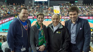 Drei Männer und eine Frau, im Hintergrund ein Volleyball-Feld und volle Zuschauerränge