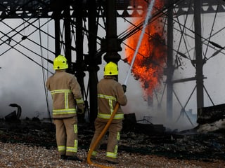 Zwei Feuerwehrleute spritzen Wasser auf den Pier