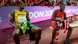 Usain Bolt und Justin Gatlin sitzend lachen nebeneinander auf einem Stuhl.